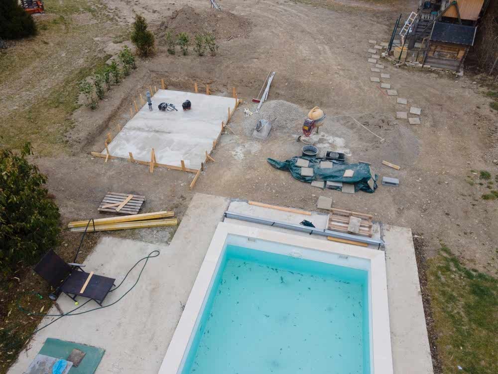 Drone shot of pool construction site with concrete pad for heat pump and pool house in garden in austria
